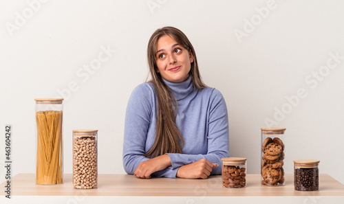 Young caucasian woman sitting at a table with food pot isolated on white background dreaming of achieving goals and purposes
