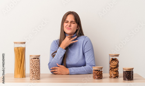 Young caucasian woman sitting at a table with food pot isolated on white background suffers pain in throat due a virus or infection.