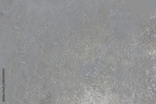 The weathered surface of the chipboard sheet, faded under the sun. Mottled structure with fine speckles.