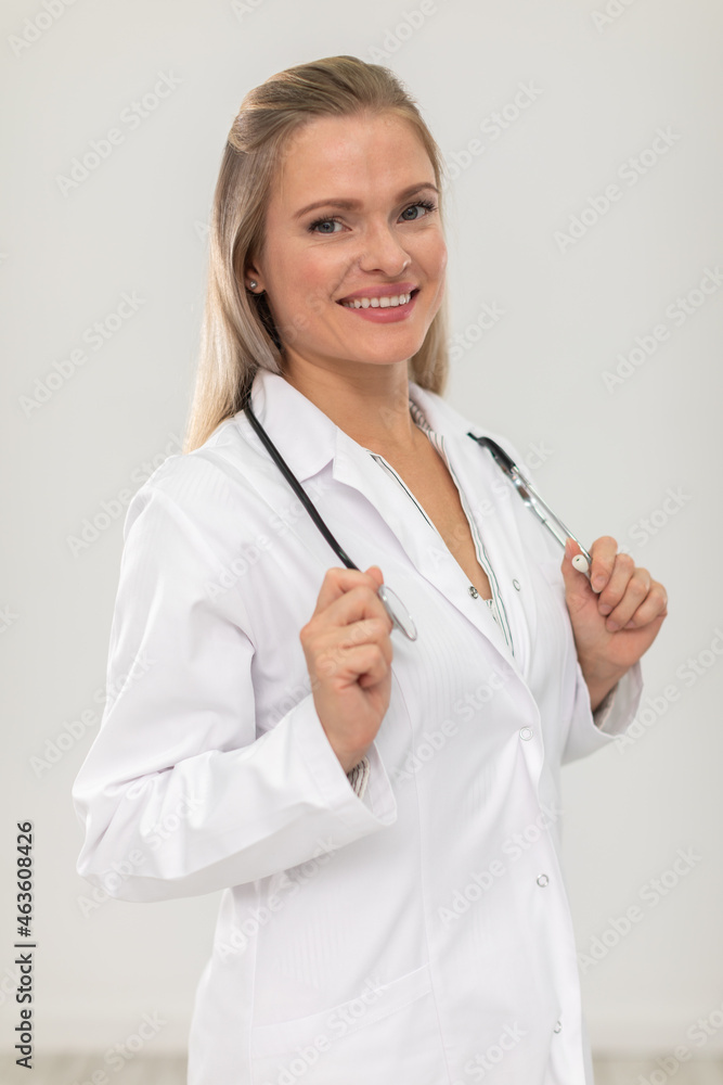 A smiling doctor stands facing the camera and holds a stethoscope in her hands. A smiling doctor stands facing the camera and holds a stethoscope in her hands.