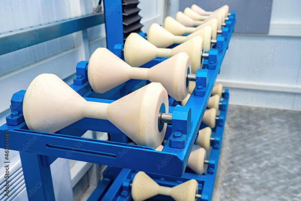 Fototapeta premium Roller supports for pipes. Tube roller tables close-up. Cones for moving and rotating round piles. Conical roller conveyors on blue supports. Equipment for working with pipes.