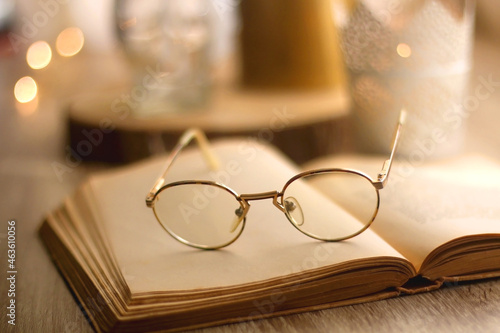 Open book, reading glasses, various candles and vase with flowers. Hygge at home. Selective focus.