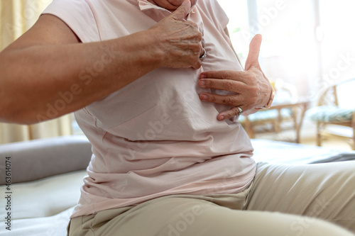 Senior woman hand checking lumps on her breast for signs of breast cancer on gray background. Healthcare concept. Caucasian woman palpating her breast by herself that she concern about breast cancer