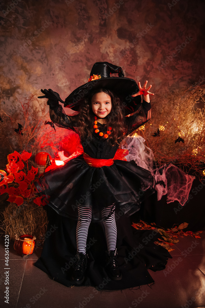 A little girl in a witch costume on a gloomy background scares people. Getting ready for All Saints Day. Halloween costume. A little girl in a witch costume on a gloomy background scares people. Getting ready for All Saints Day. Halloween costume.