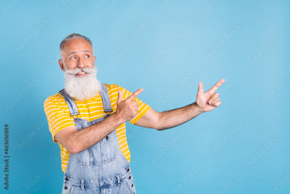 Photo of funny old white man point look empty space wear yellow t-shirt overall isolated on blue color background