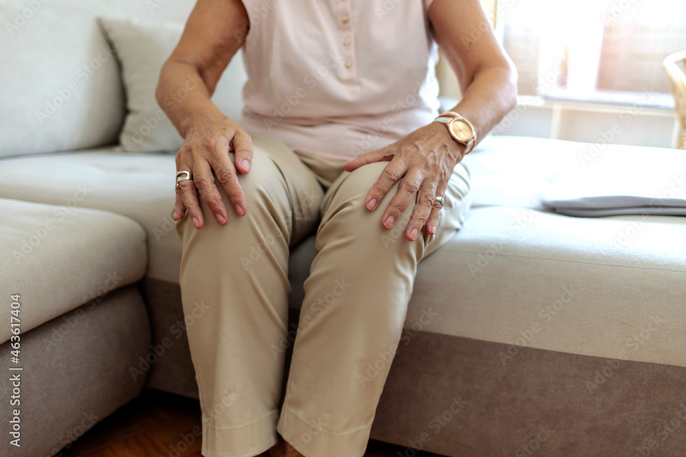 Old senior adult woman female hands touching knee sitting alone. Retired elderly grandma feeling hurt joint pain in leg suffering from osteoarthritis bones disease or injury concept, close up.