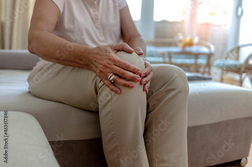 Old senior adult woman female hands touching knee sitting alone. Retired elderly grandma feeling hurt joint pain in leg suffering from osteoarthritis bones disease or injury concept, close up. photo