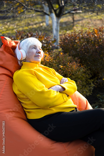 Attractive gray-haired 85 year old woman sits on a bag chair and listens to music on headphones. photo