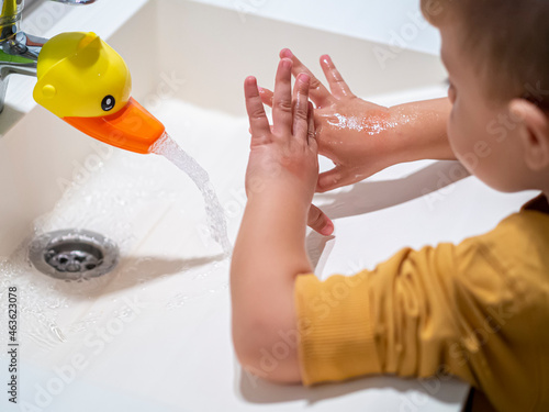 Kid washing hands in a bathroom sink at home after playing with duck toy as a faucet. Fun faucet for children for learning handwashing daily. Hygiene and daily prevention for toddlers