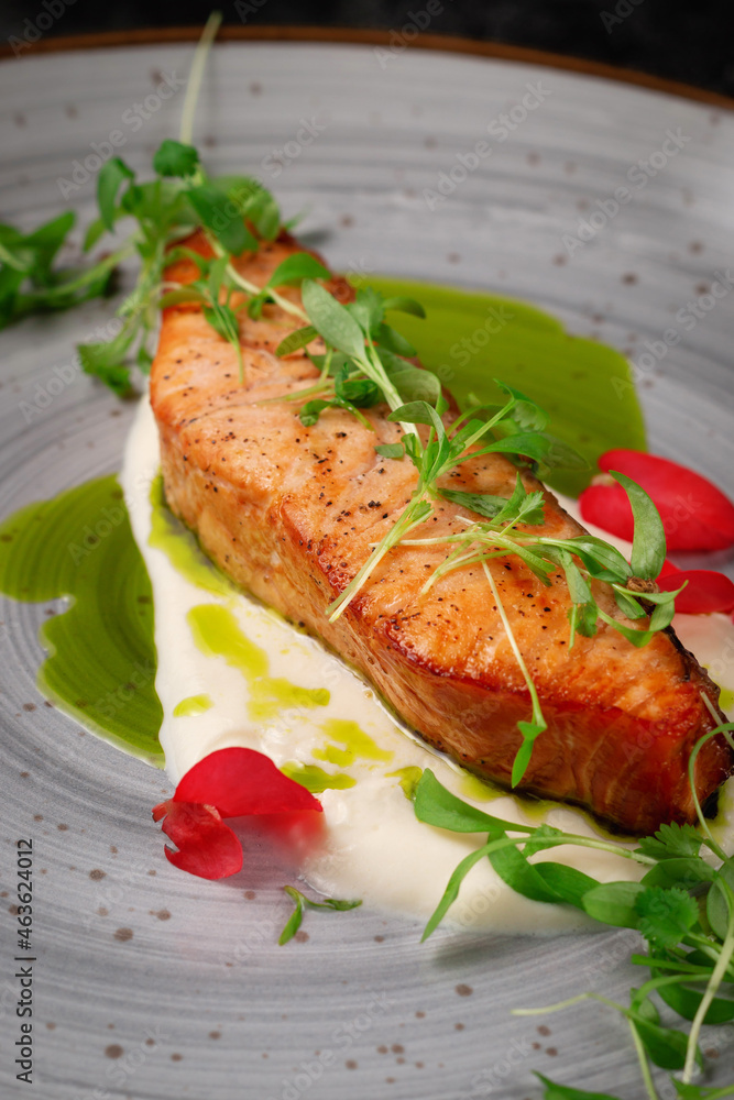 Grilled salmon steak with spices and a sprig of peas on a dark stone table Grilled salmon steak with spices and a sprig of peas on a dark stone table