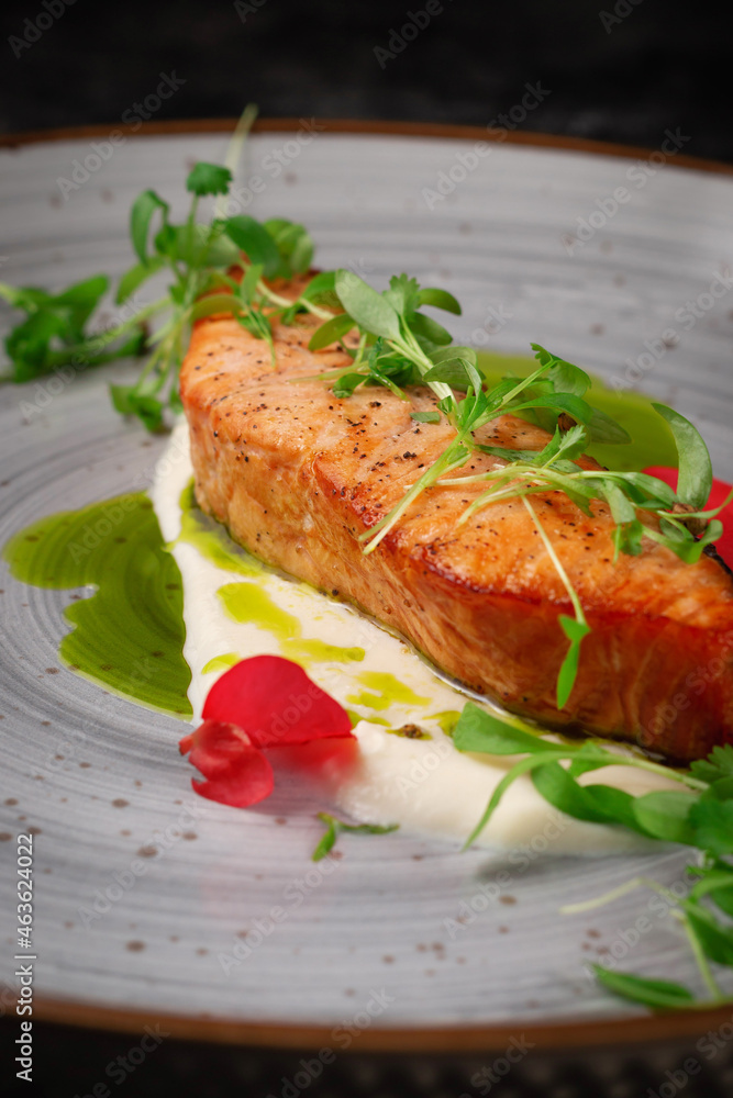 Grilled salmon steak with spices and a sprig of peas on a dark stone table