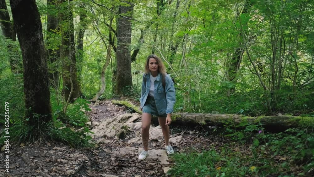A young Caucasian woman walks along a forest mountain road. Casual blue denim clothes and backpack. The theme of travel, healthy lifestyle and freedom. A young Caucasian woman walks along a forest mountain road. Casual blue denim clothes and backpack. The theme of travel, healthy lifestyle and freedom.