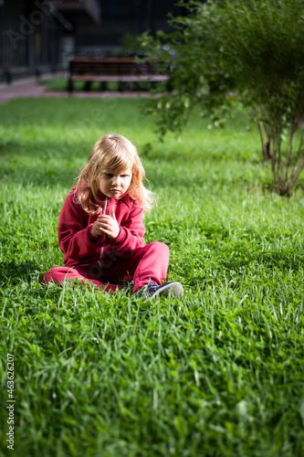 Little cute girl 5 years old blonde in red clothes on the grass, happy childhood.