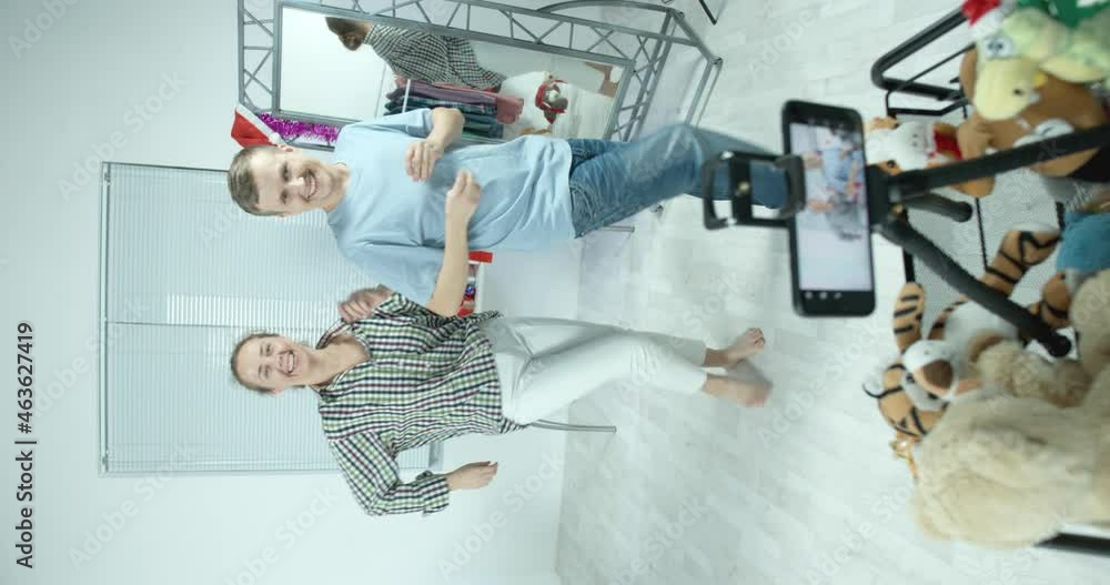 people are dancing at home. a guy and a girl, a man and a woman dance synchronously and film themselves on the phone. gifts in the background lie on the table. New Year Christmas people are dancing at home. a guy and a girl, a man and a woman dance synchronously and film themselves on the phone. gifts in the background lie on the table. New Year Christmas