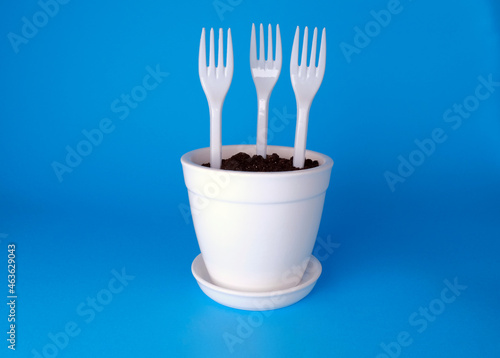 
Plastic forks in a white flower pot on a blue background. Plastic in the ground
