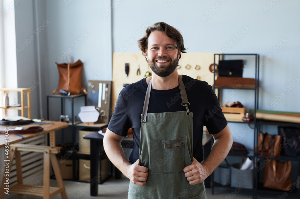 Waist up portrait of male artisan wearing apron and smiling at camera while posing in tanners workshop, copy space