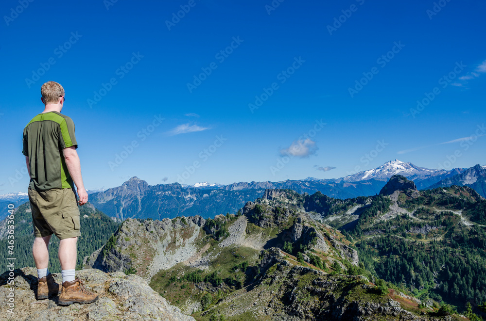 An athletic adventurous male hiker standing on top of a mountain looking out at a mountain range.