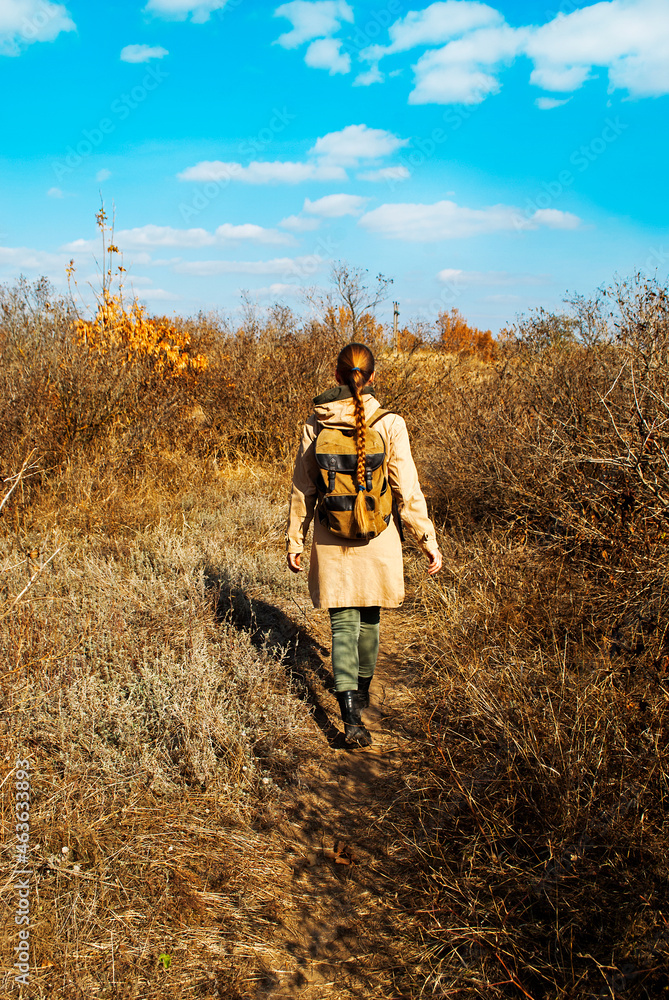 Autumn portrait of a girl outdoors. Back view. Unrecognizable woman traveler with backpack enjoying the view. 