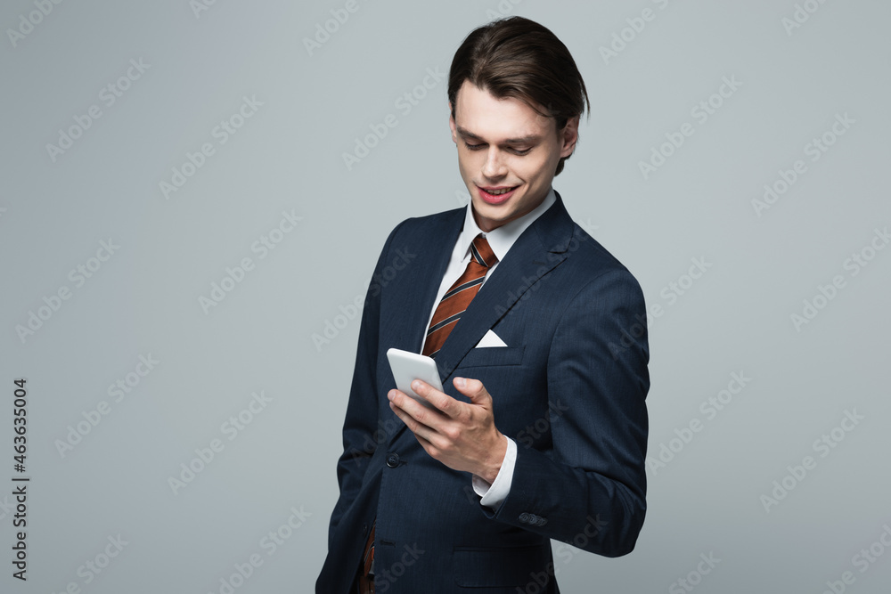 cheerful young businessman in suit using smartphone isolated on grey cheerful young businessman in suit using smartphone isolated on grey