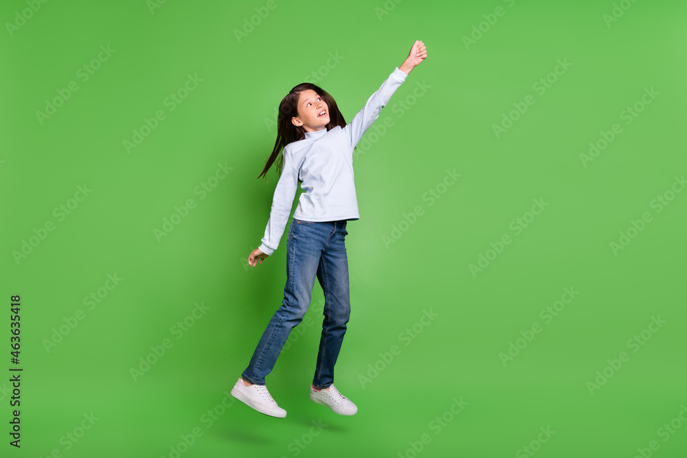 Photo of pretty funny school girl dressed blue turtleneck smiling jumping high looking empty space isolated green color background Photo of pretty funny school girl dressed blue turtleneck smiling jumping high looking empty space isolated green color background