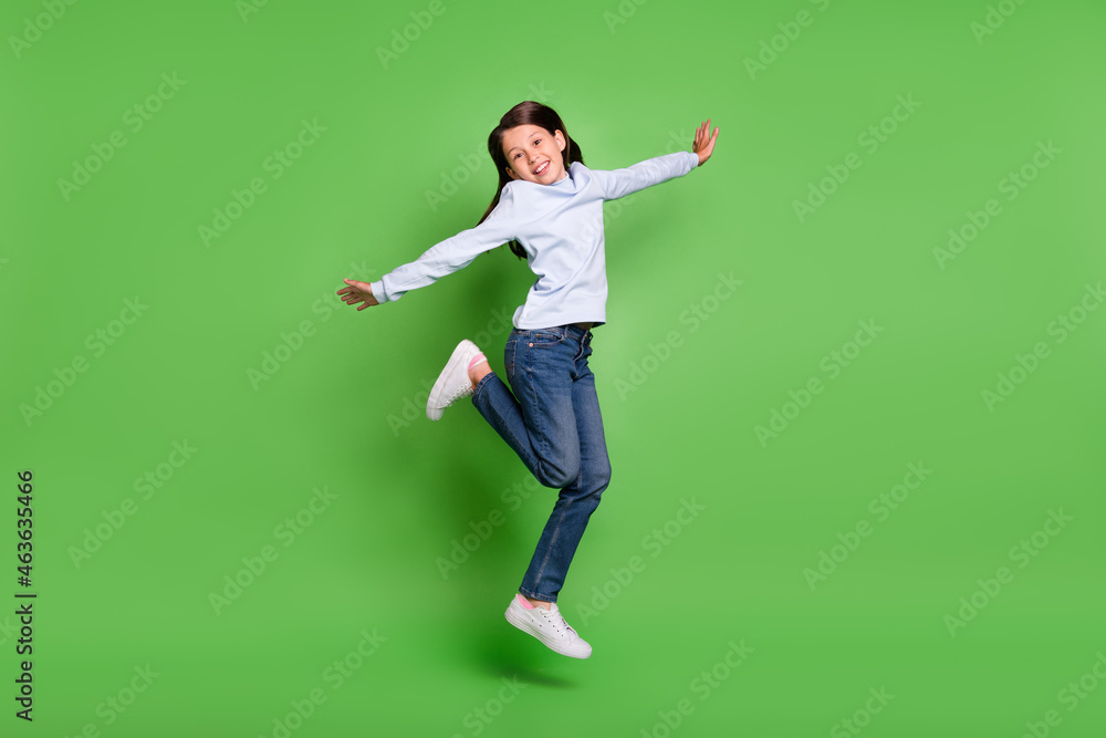 Photo of cute beautiful schoolgirl wear blue turtleneck jumping high arms sides smiling isolated green color background Photo of cute beautiful schoolgirl wear blue turtleneck jumping high arms sides smiling isolated green color background