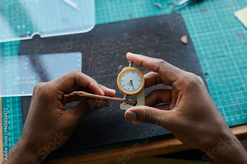 Top view of unrecognizable African-American man creating handmade leather bag while working in leatherworkers workshop, copy space photo