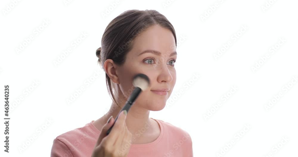 Portrait of young european woman making blush or powder on the face using makeup brush. Woman with green eyes makes makeup on the white background. Beauty, health and cosmetics. Skin care concept. Portrait of young european woman making blush or powder on the face using makeup brush. Woman with green eyes makes makeup on the white background. Beauty, health and cosmetics. Skin care concept.