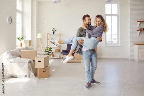 Happy young married couple on threshold of new life. Newlyweds having fun in big new home. Strong man carrying his woman in arms in newly bought modern spacious unfurnished house. Real estate concept © Studio Romantic