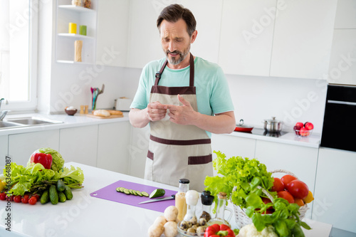 Photo of troubled man suffer cut finger feel pain hurt wear kitchenware apron in kitchen apartment indoors