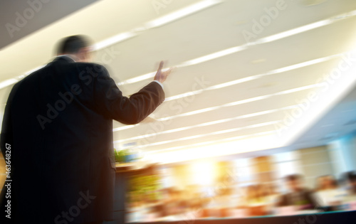Business man is making a speech in front of a big audience at a conference hall..