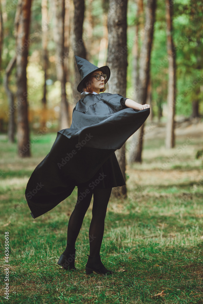 Halloween Witch. Portrait of a girl in a hat and a witch costume in the forest. Ready for trick or treat holiday