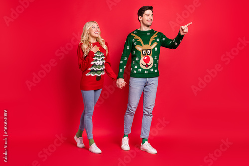 Full length body size photo couple holding hands walking pointing copyspace isolated vibrant red color background © deagreez