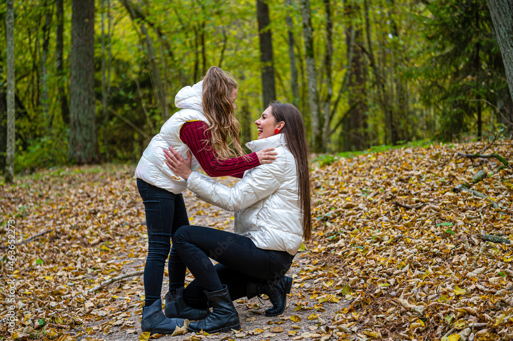 Fototapeta premium two sisters dressed in light jackets walk in the park in autumn, talk and share secrets