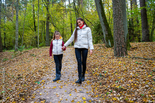 two sisters holding hands, dressed in light jackets, walking in the park in autumn