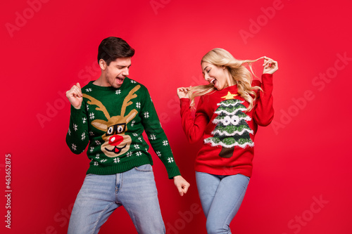 Photo of cute charming young couple dressed ugly print sweaters smiling dancing isolated red color background