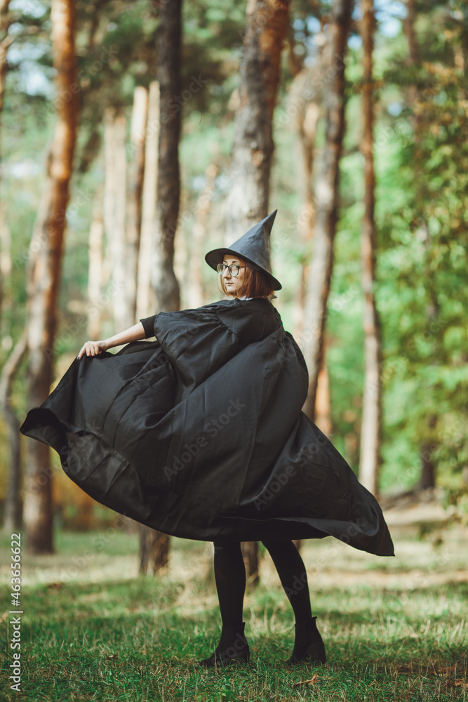 Halloween Witch. Portrait of a girl in a hat and a witch costume in the forest. Ready for trick or treat holiday