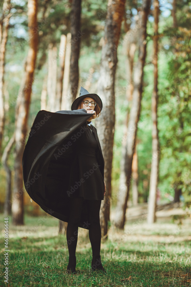 Halloween Witch. Portrait of a girl in a hat and a witch costume in the forest. Ready for trick or treat holiday