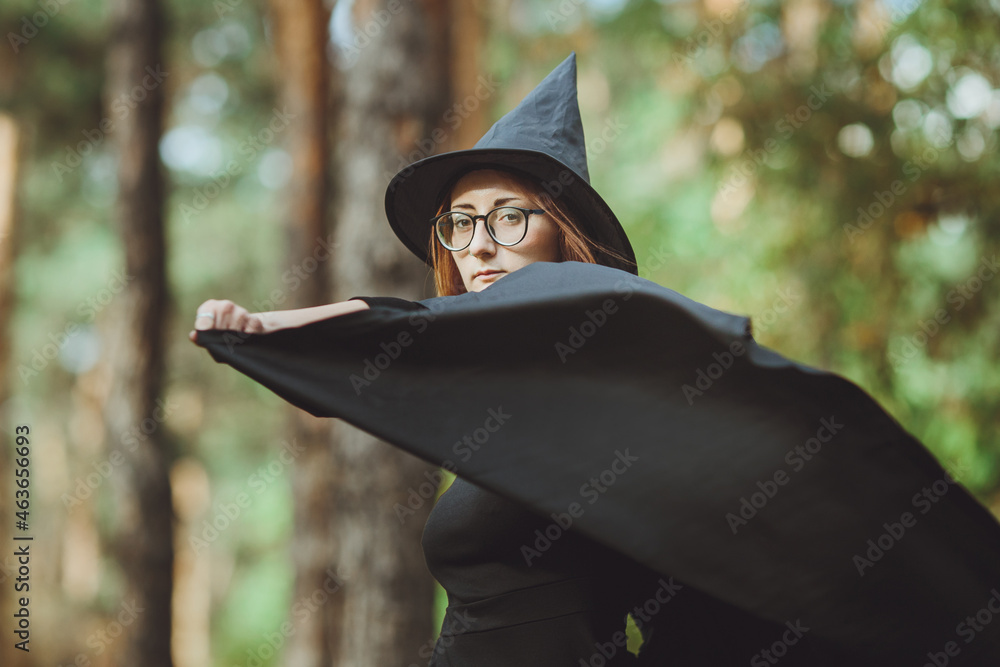 Halloween Witch. Portrait of a girl in a hat and a witch costume in the forest. Ready for trick or treat holiday