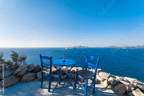 Fototapeta Naklejka Na Ścianę i Meble -  Outdoor blue chairs and desk at the cliff edge against blue Aegean sea, Santorini Island, Greece