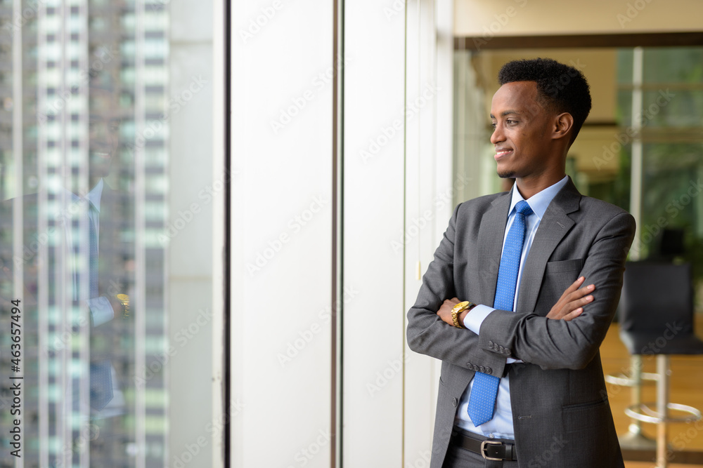 Portrait of handsome African businessman looking through window while thinking Portrait of handsome African businessman looking through window while thinking