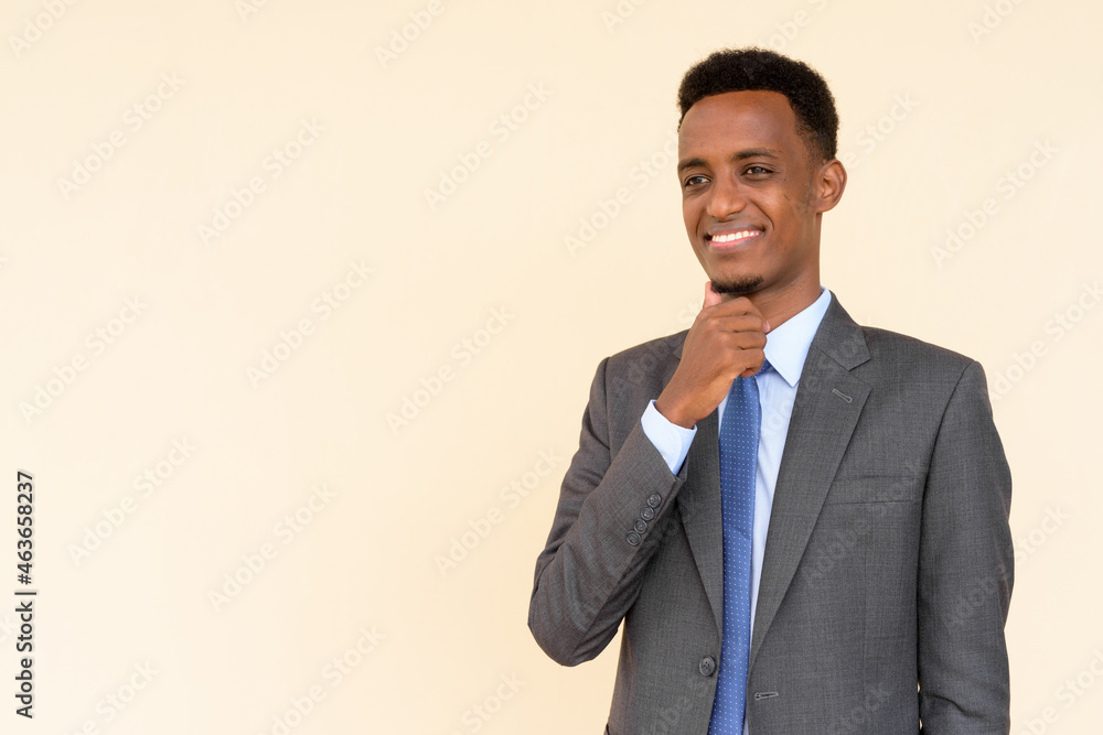 Portrait of happy thoughtful African businessman wearing suit and tie against plain background while thinking Portrait of happy thoughtful African businessman wearing suit and tie against plain background while thinking