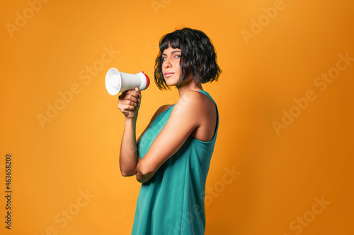 Obraz na plátně Pretty European woman wearing a teal tank top talking loud on a megaphone agains