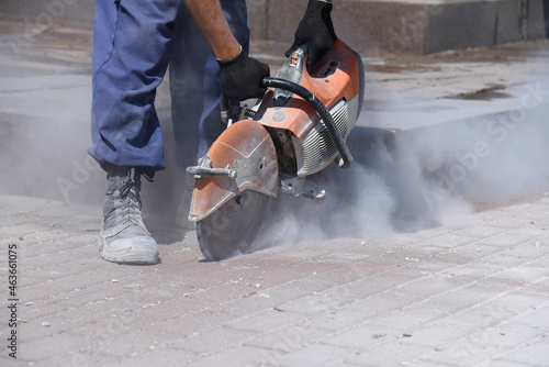 A worker cuts asphalt with a circular saw, a planned replacement of a pipe in the road surface.