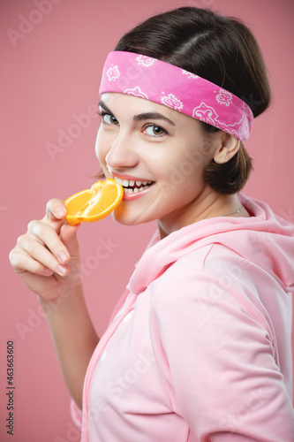 Beauty portrait of a young woman standing isolated over pink background, showing slices of an orange