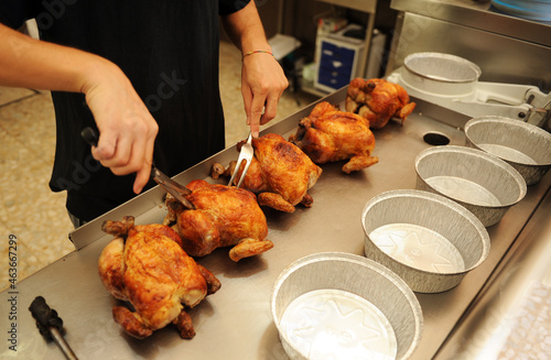 Trinchando los pollos asados en el asador de pollos. Empleado del asador de pollos preparando los pollos para servir los pedidos
