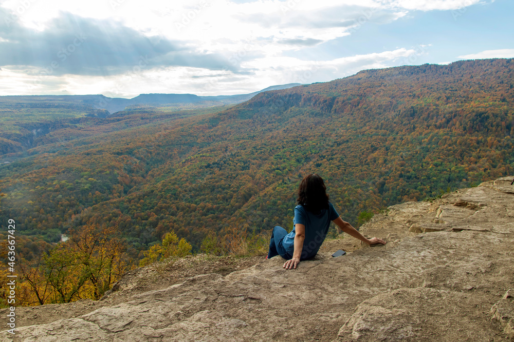 A woman enjoys the scenic views from the edge of a cliff in the stunning backdrop. Back view.