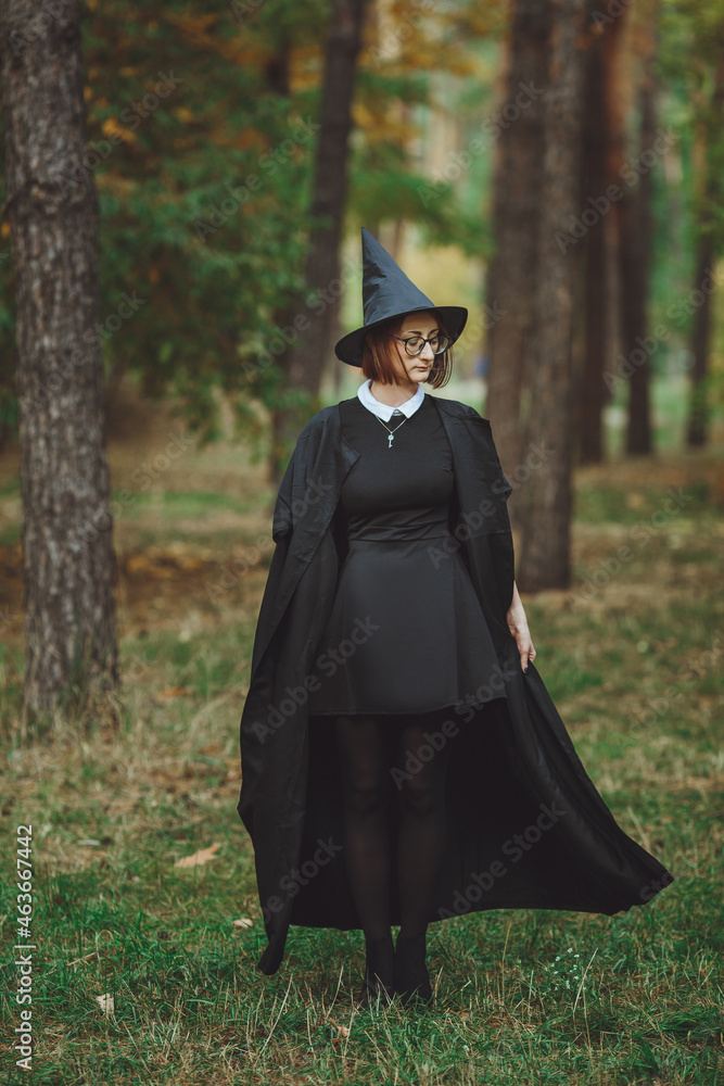 Halloween Witch. Portrait of a girl in a hat and a witch costume in the forest. Ready for trick or treat holiday