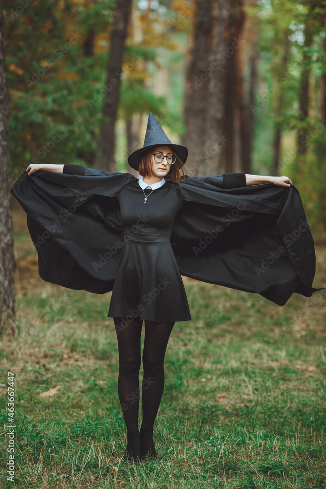 Halloween Witch. Portrait of a girl in a hat and a witch costume in the forest. Ready for trick or treat holiday