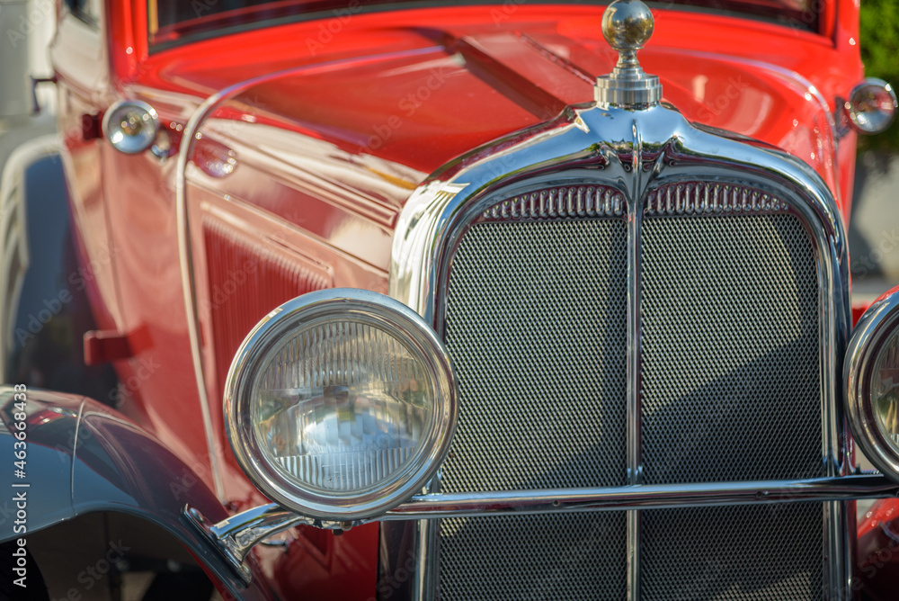 Details of the front and round headlight of a red classic car
