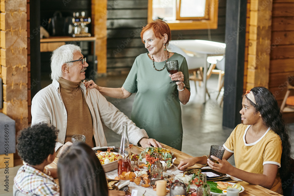Happy grandparent sitting at dining table together with grandchildren and celebrating event at home Happy grandparent sitting at dining table together with grandchildren and celebrating event at home